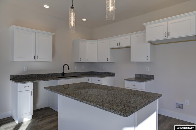 kitchen with dark hardwood / wood-style floors, decorative light fixtures, white cabinetry, sink, and a center island