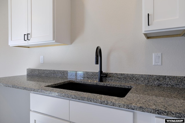 kitchen with white cabinetry, stone countertops, and sink