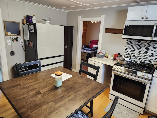 kitchen featuring stainless steel gas stove, decorative backsplash, white cabinets, and refrigerator