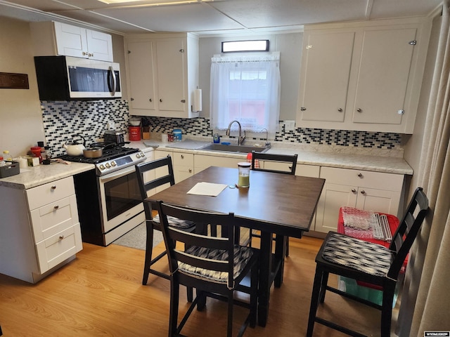 kitchen featuring appliances with stainless steel finishes, sink, white cabinets, decorative backsplash, and light wood-type flooring