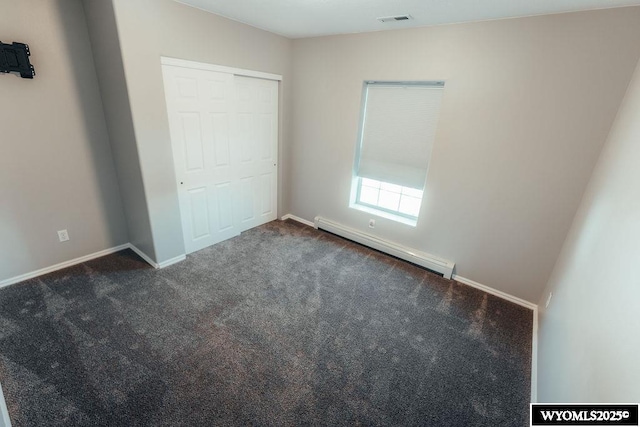 unfurnished bedroom featuring dark colored carpet, baseboard heating, and a closet