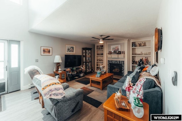 living room with ceiling fan, a fireplace, light hardwood / wood-style floors, a textured ceiling, and built in shelves