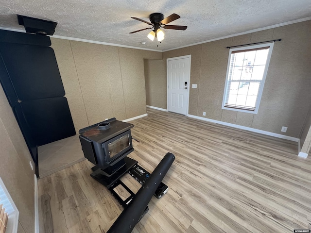 exercise room featuring a wood stove, light wood-type flooring, ornamental molding, ceiling fan, and a textured ceiling