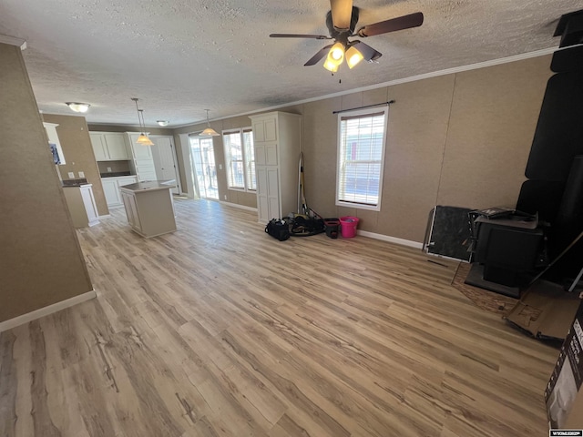 unfurnished living room featuring a textured ceiling, a wood stove, ornamental molding, ceiling fan, and light hardwood / wood-style floors