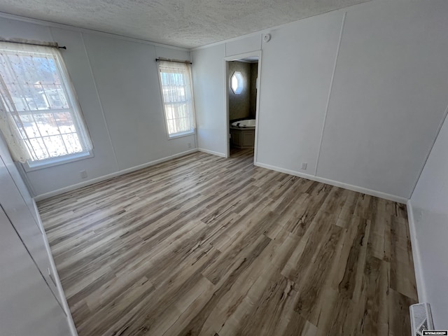 spare room with a healthy amount of sunlight, a textured ceiling, and light hardwood / wood-style floors