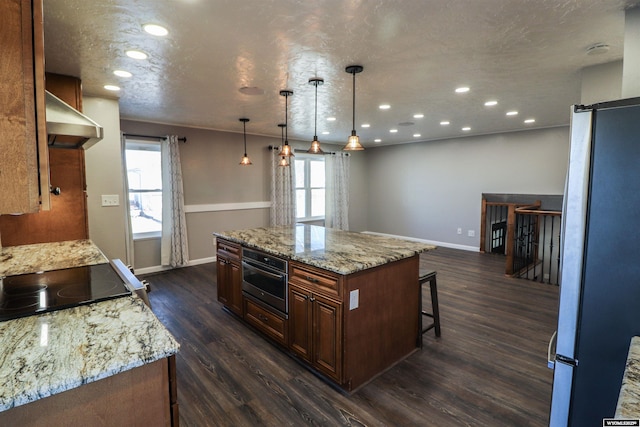 kitchen featuring appliances with stainless steel finishes, dark hardwood / wood-style floors, decorative light fixtures, a center island, and wall chimney exhaust hood