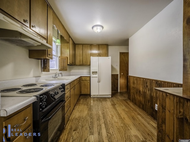 kitchen featuring black electric range oven, sink, light hardwood / wood-style flooring, white refrigerator with ice dispenser, and wood walls