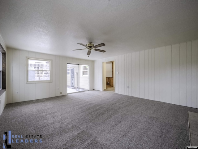 empty room featuring carpet floors, wooden walls, and ceiling fan