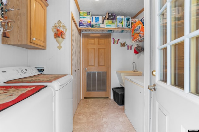 clothes washing area featuring cabinets, sink, washing machine and clothes dryer, and a textured ceiling