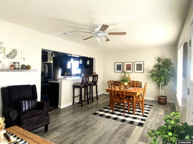 dining space with baseboards, a textured ceiling, ceiling fan, and dark wood-style flooring