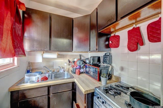 kitchen with dark brown cabinetry, range with gas stovetop, sink, and backsplash