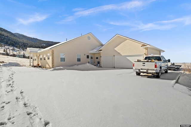 snow covered rear of property with a mountain view and a garage