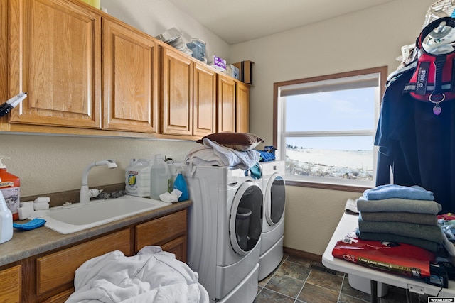 washroom with a sink, stone finish flooring, washer and dryer, cabinet space, and baseboards