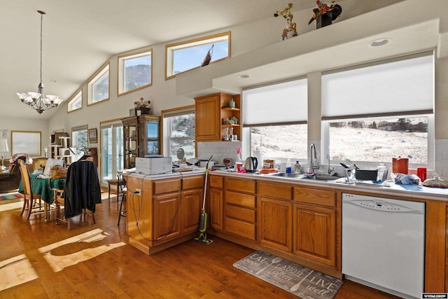 kitchen featuring a peninsula, white dishwasher, a sink, dark wood-type flooring, and a notable chandelier