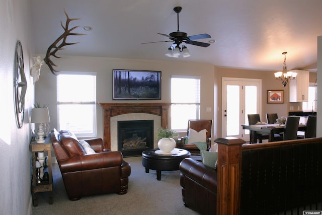 carpeted living room featuring ceiling fan with notable chandelier and a tile fireplace