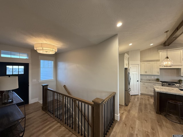 hallway with lofted ceiling, light hardwood / wood-style floors, and a textured ceiling