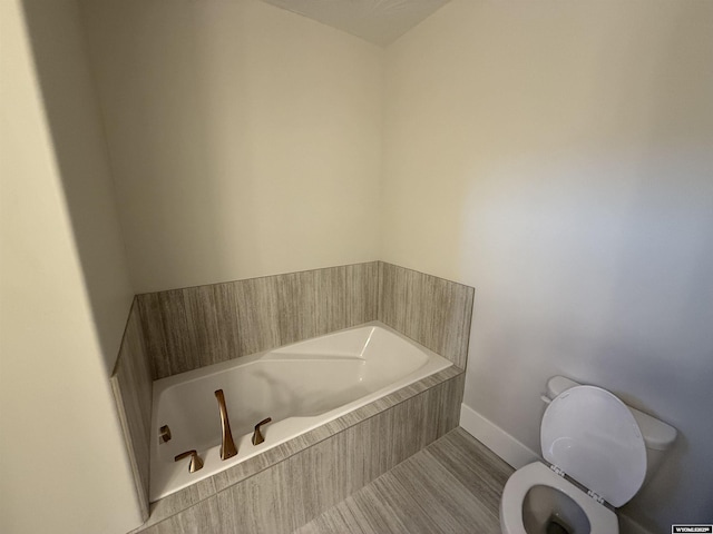 bathroom featuring tiled tub and toilet