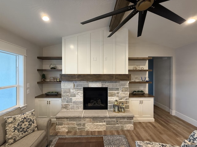 living room featuring a stone fireplace, vaulted ceiling, ceiling fan, and light wood-type flooring