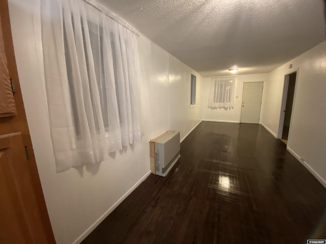 corridor featuring heating unit, dark wood-type flooring, and a textured ceiling