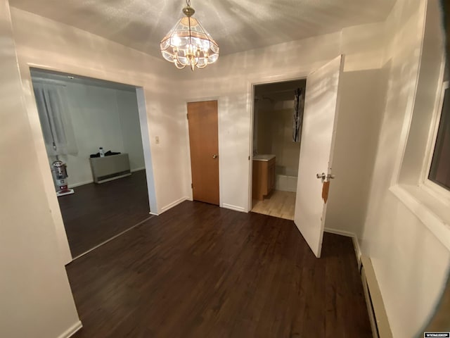 unfurnished bedroom featuring dark wood-type flooring, ensuite bath, and a notable chandelier