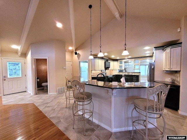 kitchen featuring pendant lighting, tasteful backsplash, stainless steel fridge, a kitchen breakfast bar, and beamed ceiling