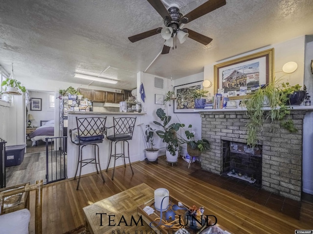 living room with dark wood-type flooring, ceiling fan, a brick fireplace, and a textured ceiling