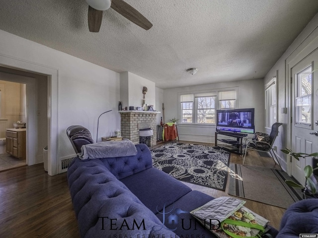 living room featuring dark hardwood / wood-style flooring, a brick fireplace, a textured ceiling, and ceiling fan