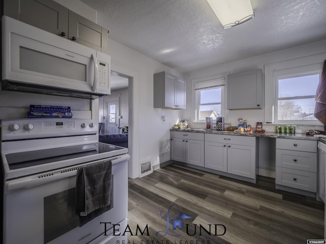 kitchen featuring white appliances, dark hardwood / wood-style floors, a textured ceiling, and stone countertops