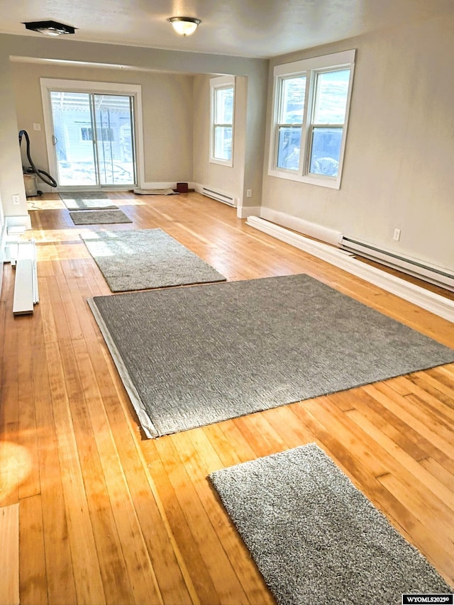 workout area with a baseboard heating unit, wood-type flooring, and baseboards