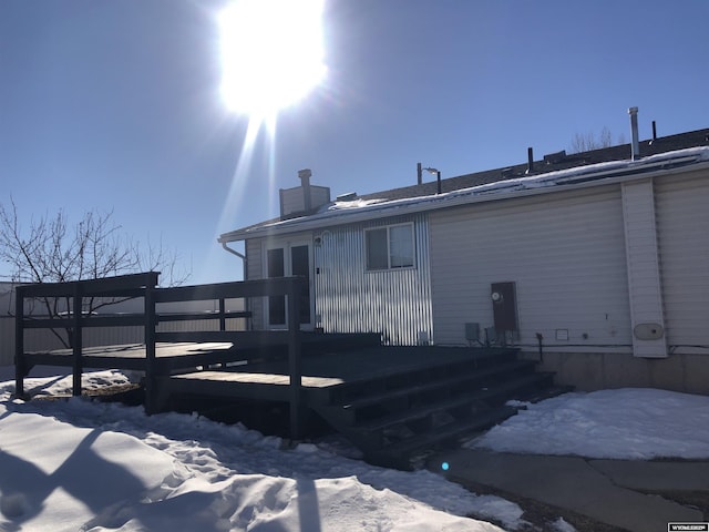 snow covered rear of property with a chimney and a wooden deck