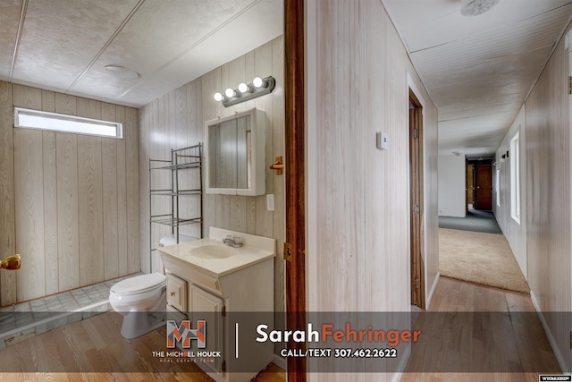 bathroom with hardwood / wood-style flooring, vanity, wood walls, and toilet