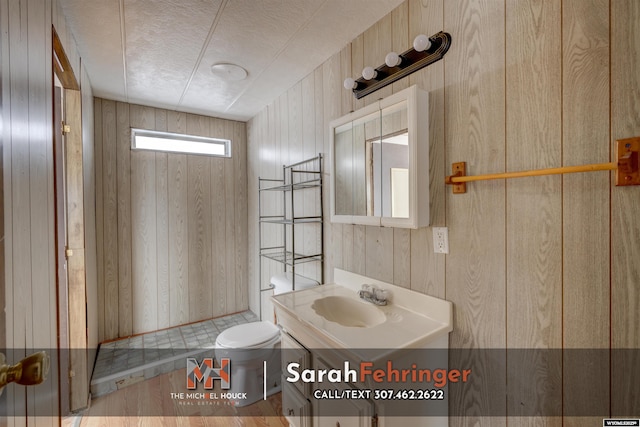 bathroom with vanity, toilet, a textured ceiling, and wood walls