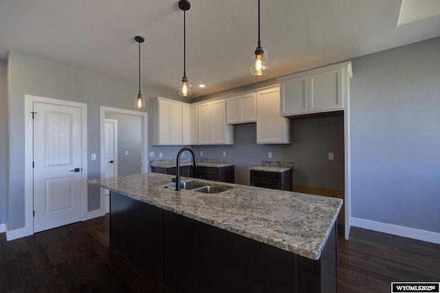 kitchen with pendant lighting, white cabinetry, an island with sink, sink, and light stone countertops