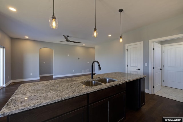 kitchen featuring dark wood-type flooring, light stone countertops, sink, and hanging light fixtures