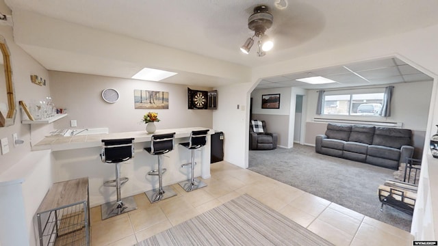 kitchen with light carpet, tile counters, a kitchen breakfast bar, and ceiling fan