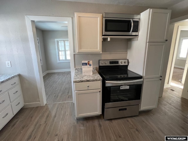 kitchen with light stone counters, hardwood / wood-style flooring, white cabinets, and appliances with stainless steel finishes