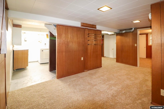 basement with washer / clothes dryer, light colored carpet, and wood walls