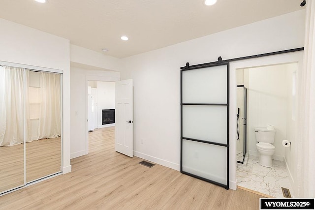 unfurnished bedroom featuring a closet, ensuite bath, light hardwood / wood-style flooring, and a barn door