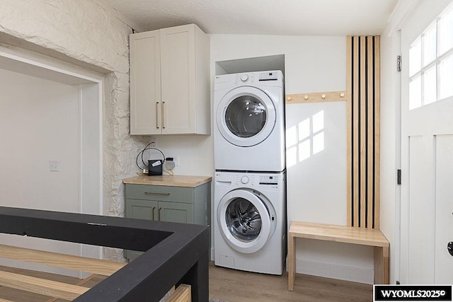 washroom with cabinets, wood-type flooring, and stacked washer / drying machine