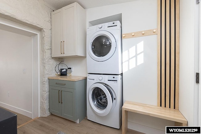 laundry room with cabinets, stacked washer and clothes dryer, and light hardwood / wood-style flooring