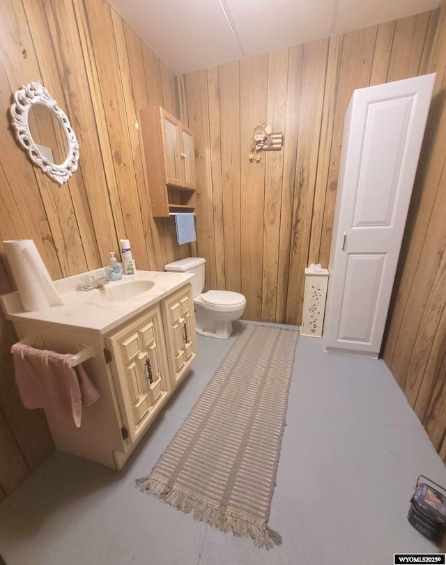 bathroom featuring vanity, wooden walls, and toilet