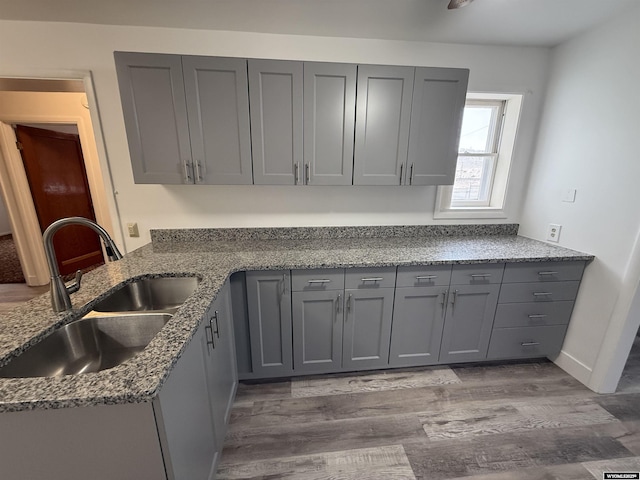 kitchen featuring sink, gray cabinetry, dark wood-type flooring, and dark stone counters