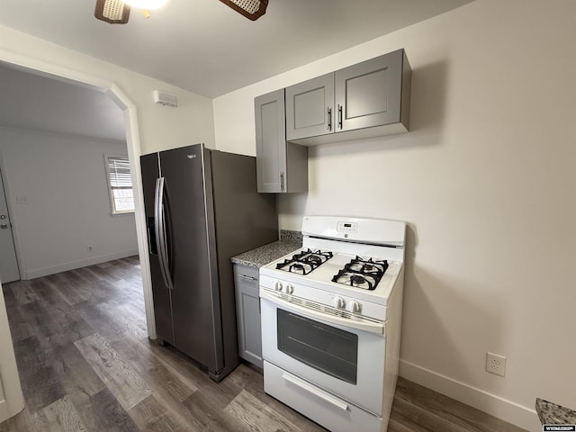 kitchen featuring dark wood-type flooring, stainless steel fridge, white range with gas cooktop, gray cabinets, and ceiling fan