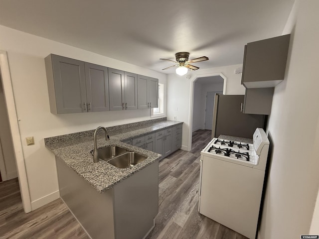 kitchen with sink, gray cabinets, stainless steel refrigerator, kitchen peninsula, and white gas stove