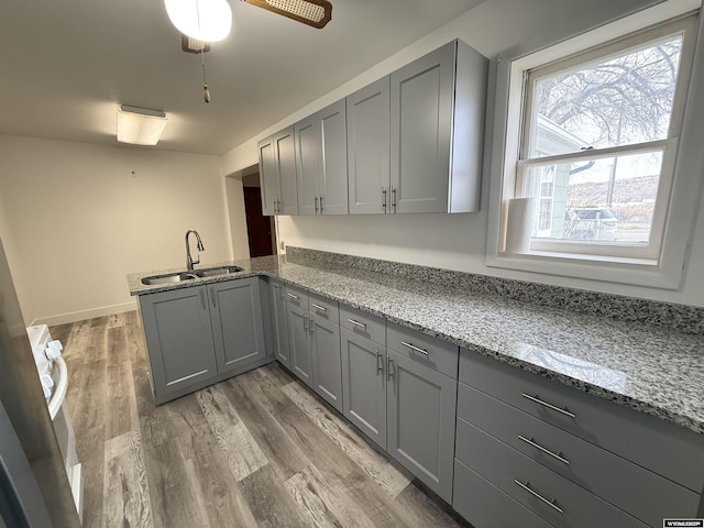 kitchen featuring sink, gray cabinets, hardwood / wood-style floors, light stone counters, and kitchen peninsula