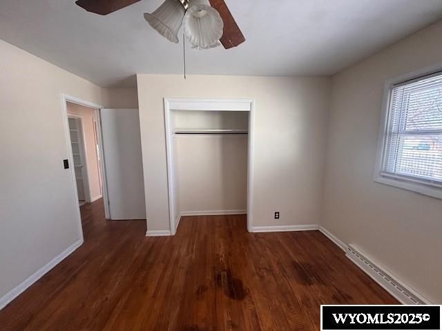 unfurnished bedroom with baseboard heating, ceiling fan, dark wood-type flooring, and a closet