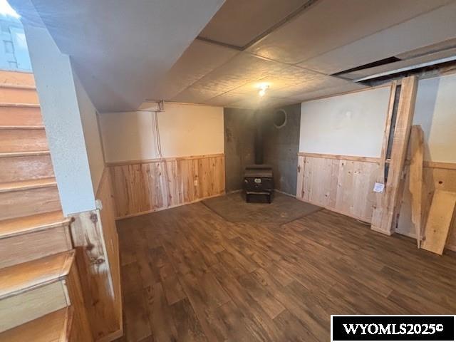 basement with a wood stove, dark wood-type flooring, and wood walls