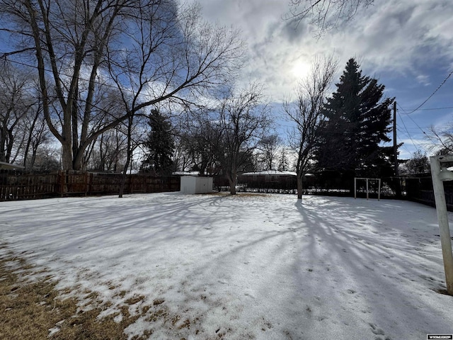 yard layered in snow featuring an outbuilding, a fenced backyard, and a shed