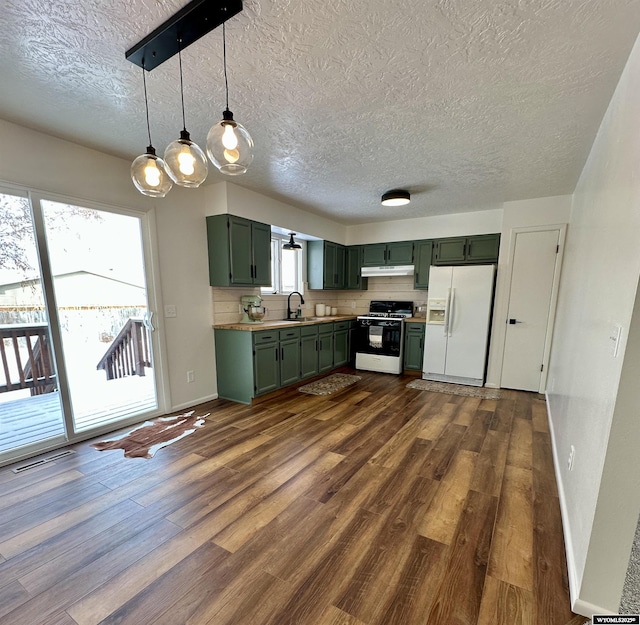 kitchen featuring gas stove, white refrigerator with ice dispenser, green cabinets, and decorative light fixtures