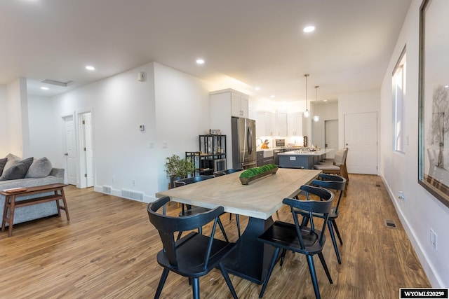 kitchen featuring a kitchen island, stainless steel refrigerator, white cabinetry, a kitchen bar, and hanging light fixtures